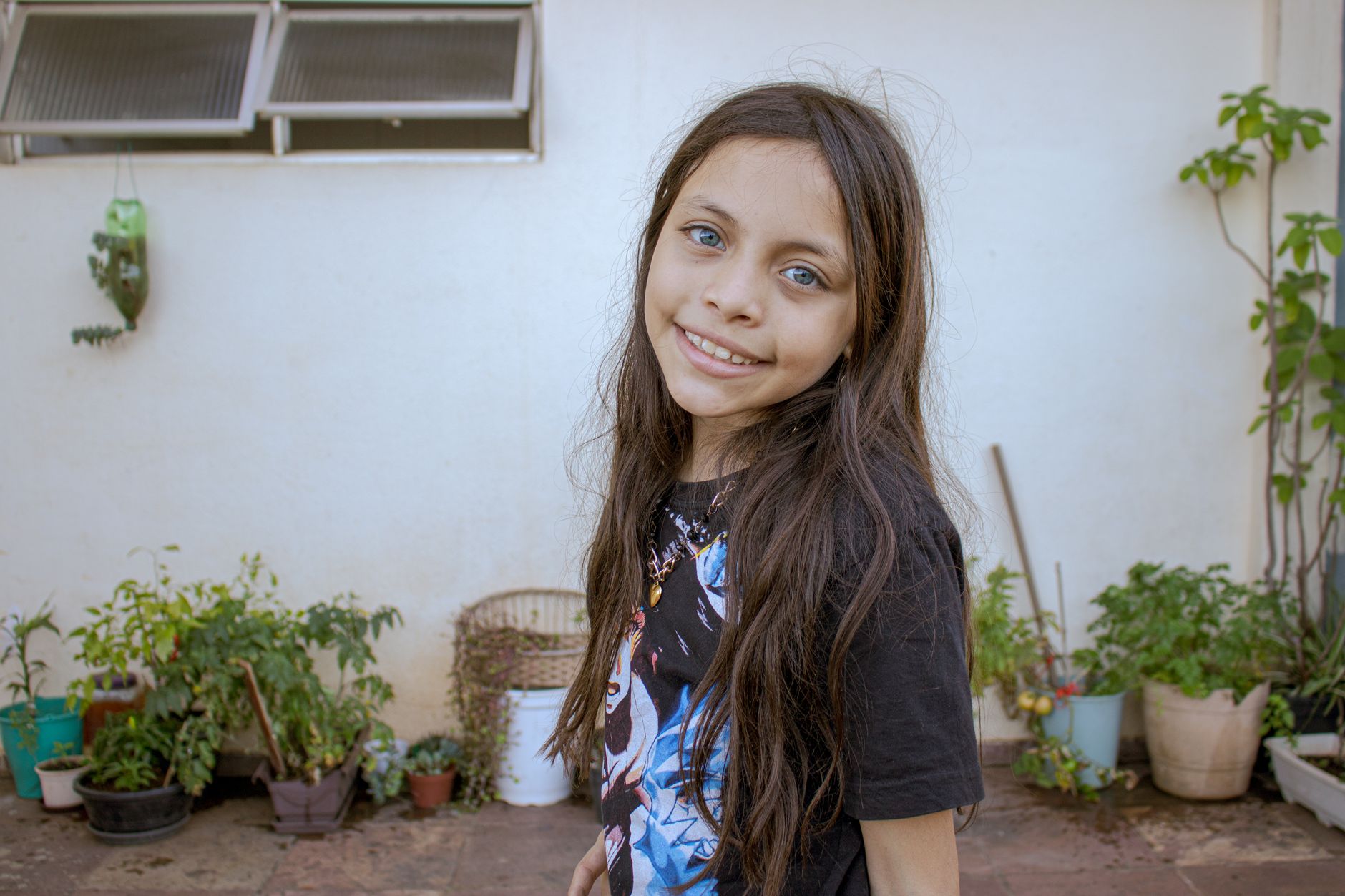 Young girl smiling in an outdoor garden area with plants in pots.