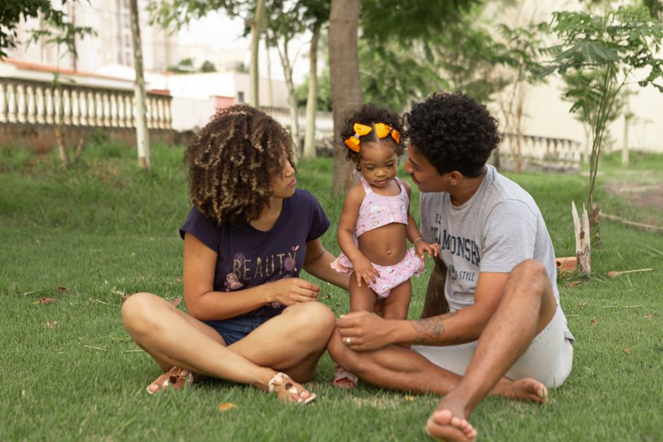 African American parents with crossed legs talking to adorable daughter while sitting on lawn in town
