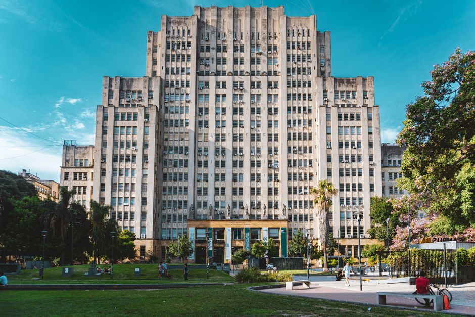 A historic university building showcasing art deco architecture with a lush park in the foreground.