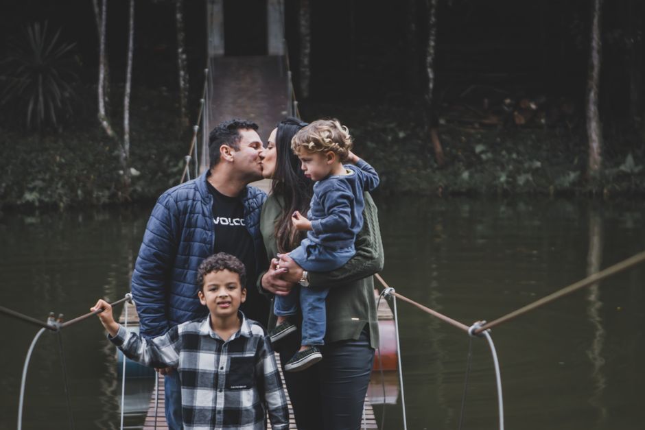 Family kissing on a suspension bridge surrounded by nature.