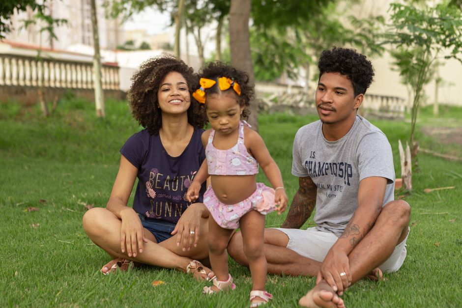 Young family enjoying quality time outdoors, sitting on grass in a park.