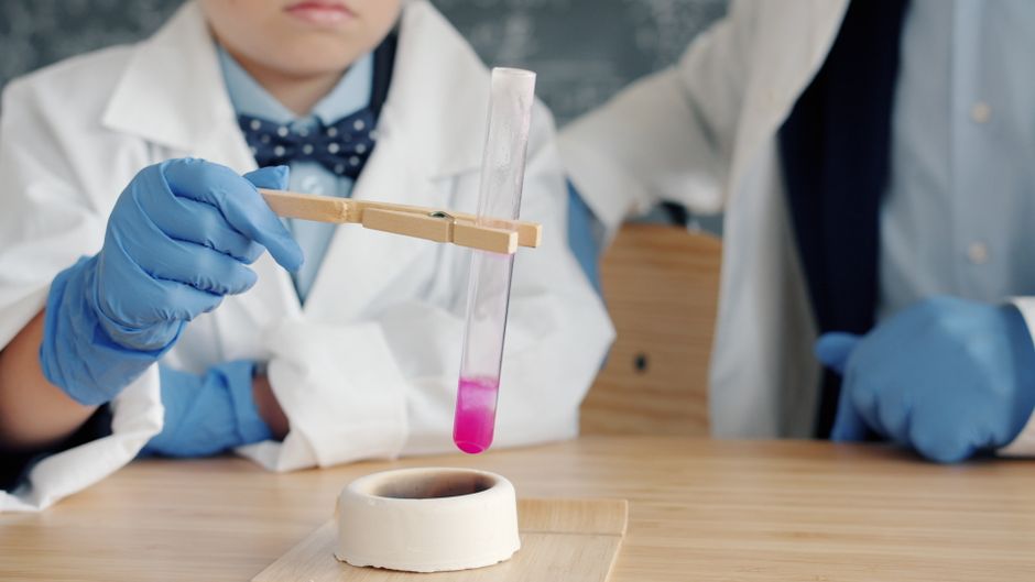 Child performs chemistry experiment with pink solution in test tube.